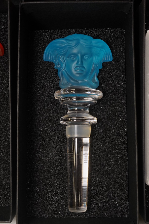 Six boxed Rosenthal for Versace glass Medusa head wine bottle stoppers in various colours and a boxed miniature timepiece, 8.5cm high (7). Condition - good.